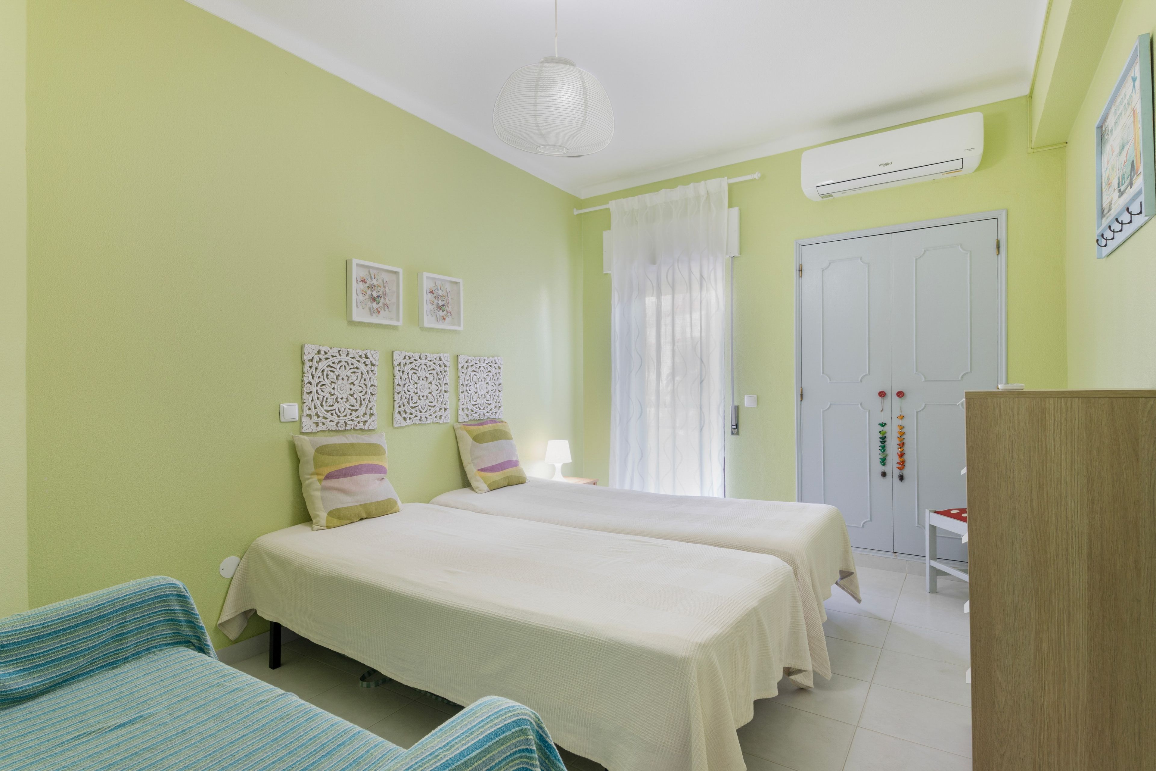 Una habitación con dos camas, un armario, una lámpara colgante y un aire acondicionado instalado en la pared.