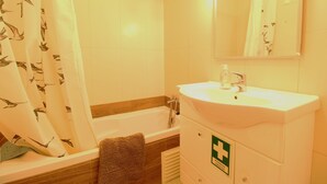A bathroom with a bathtub, a sink, and a mirror. There is a towel rack and a first aid sign on the wall. - Holiday Home 'Mantamar Beach Ap' with Balcony, Wi-Fi and Air Conditioning (Vila Nova de Cacela)