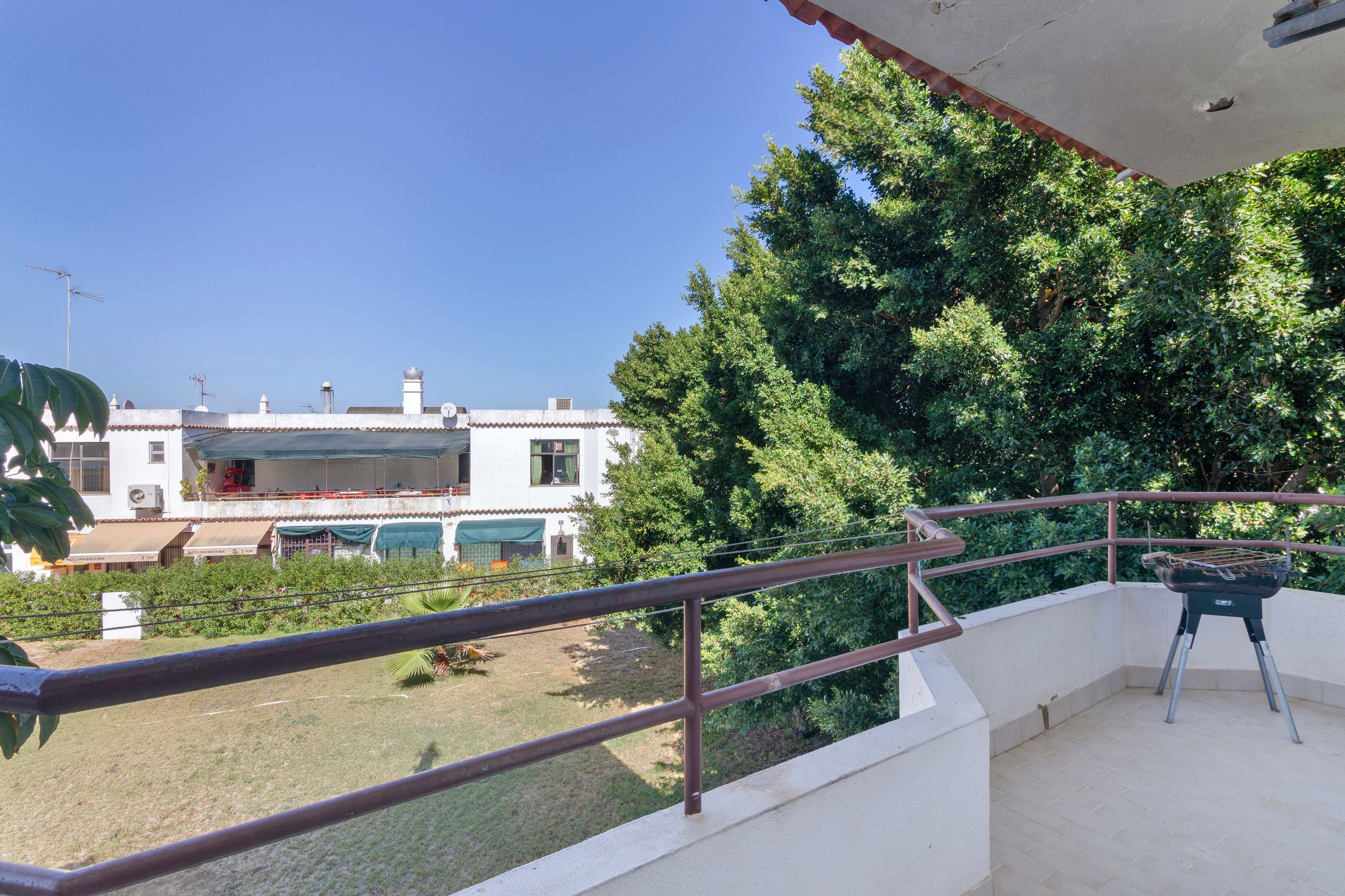 Un balcón con barandilla de metal que da a un jardín y un edificio con piscina.