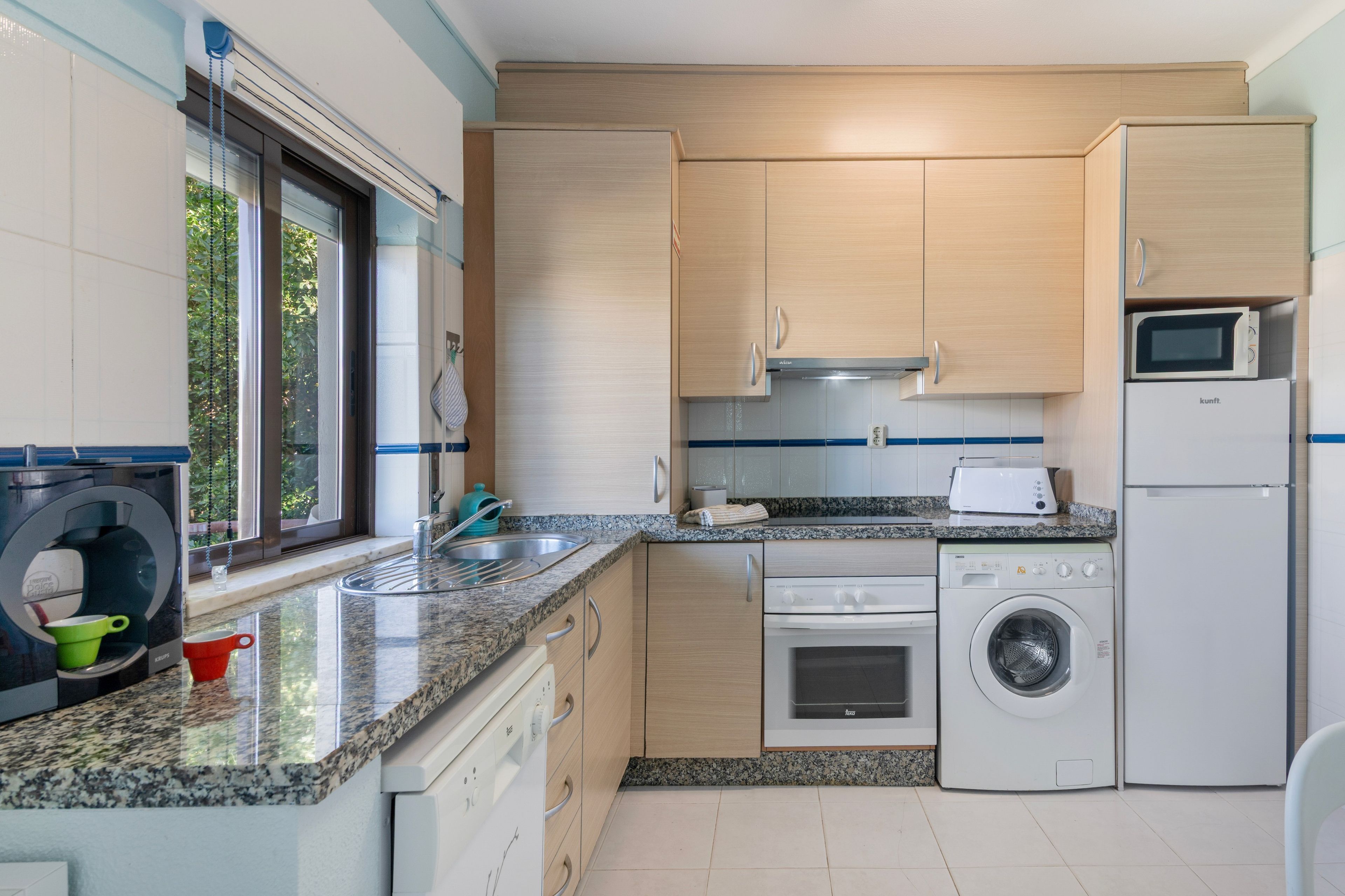 A modern kitchen with granite countertops, stainless steel appliances, and light wood cabinetry.