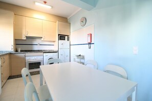 Una cocina compacta con una mesa de comedor, sillas, microondas, refrigerador y un reloj en la pared.