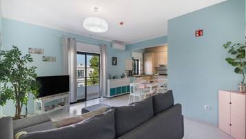 Ein modernes Wohnzimmer mit einem grauen Sofa, einem Fernseher und einem Essbereich mit Tisch und Stühlen.