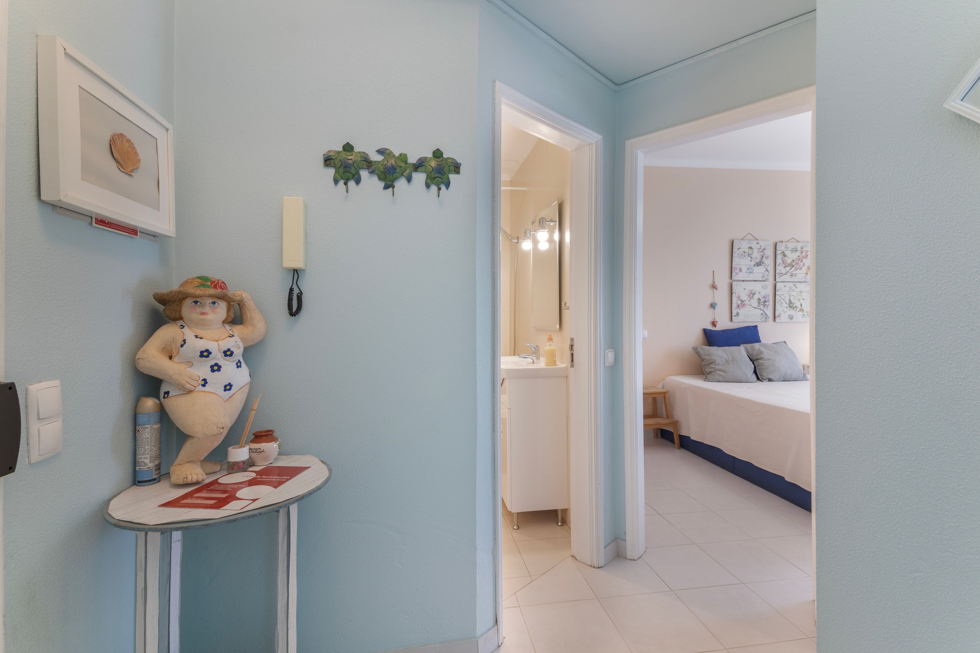 Ein Zimmer mit einem Bett, einem kleinen Tisch mit einer Figur und einem durchgehenden Türspalt sichtbaren Badezimmer.