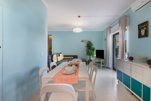 Un espace repas comprenant une table et des chaises, un canapé, un téléviseur et un coin cuisine avec des placards et une plante.