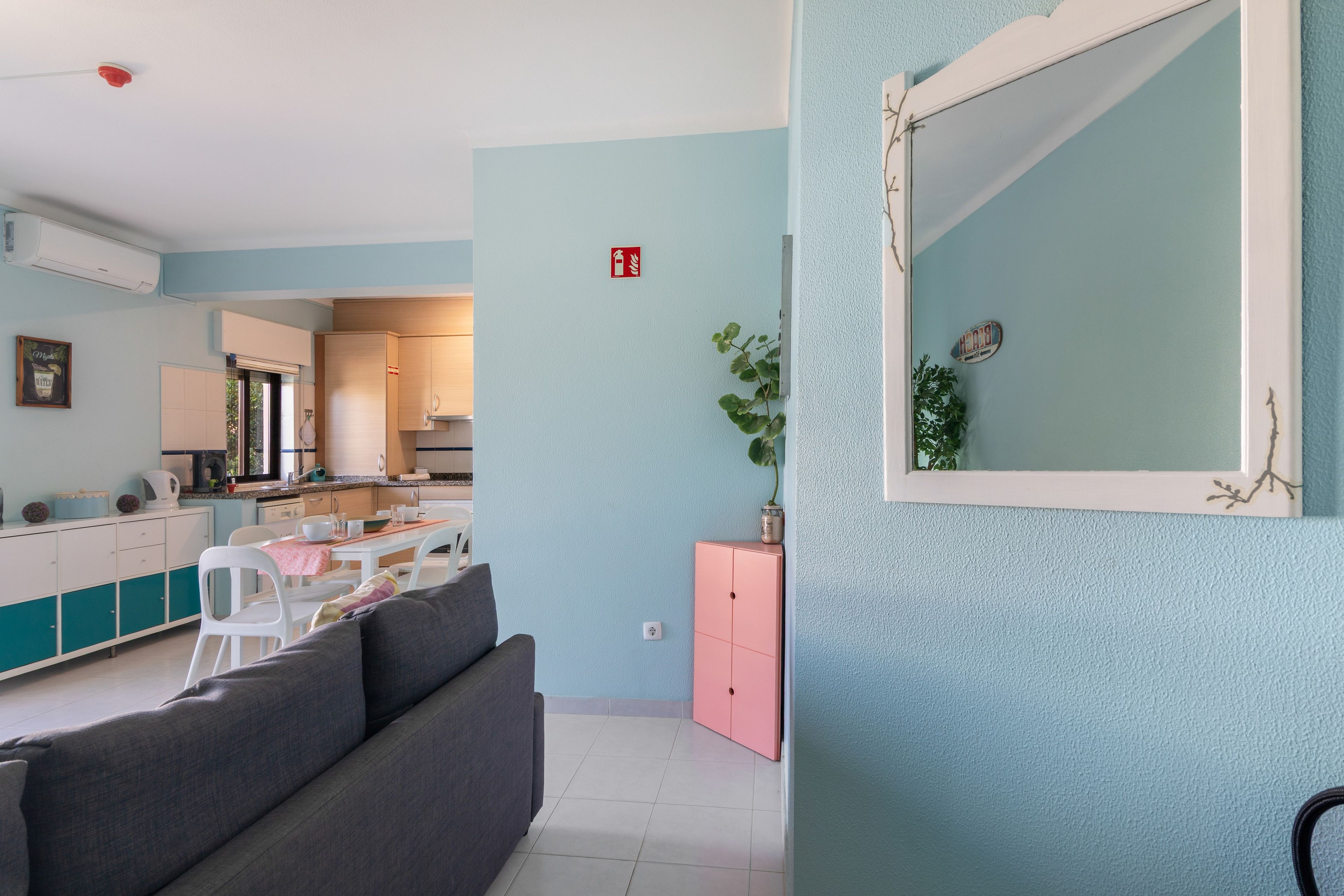 Una sala moderna con un sofá gris, un aparador rosa y un espejo grande en la pared.