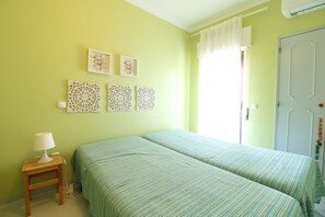 Una habitación con dos camas, una mesita de noche con lámpara, decoración en la pared y una puerta con cortina.