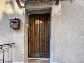 Una porta de fusta amb un mànec metàl·lic, una closca de correu i un número identificador a la paret.