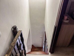 Un vestíbul estret amb escales de fusta i barana metàl·lica.
