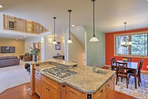 A modern kitchen with a central island, pendant lighting, and a dining area with a table and chairs. - Spacious SLT Retreat w Forest Views (South Lake Tahoe)