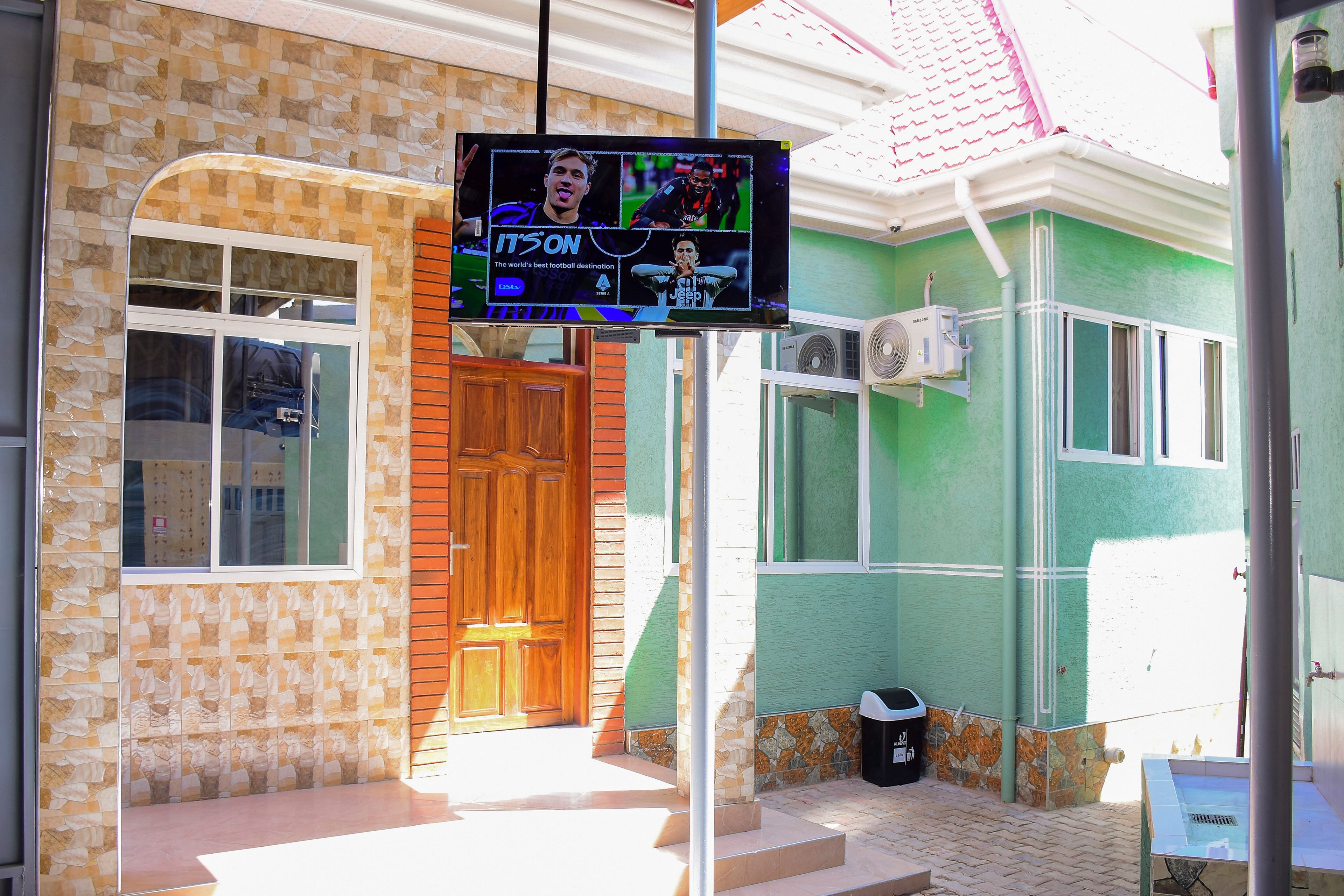 Un edificio con fachada de tejas, puerta de madera y un televisor con un evento deportivo.