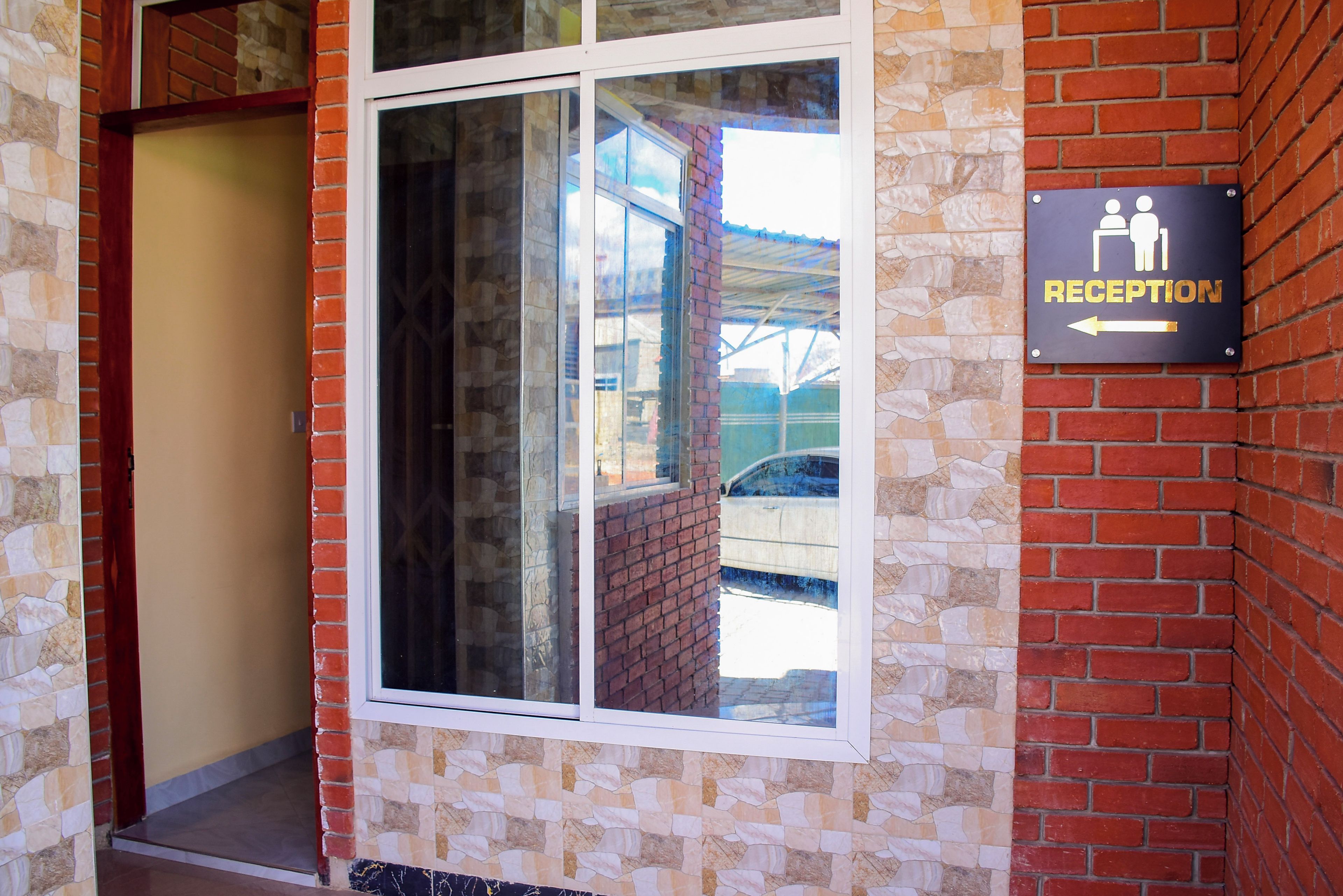 Zona de recepción con un cartel que indica la recepción, un vidrio y una pared de ladrillo.