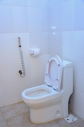 A white toilet with a closed seat, a toilet paper holder, and a bidet attachment. - FLORENTINA LODGE DODOMA (Dodoma)