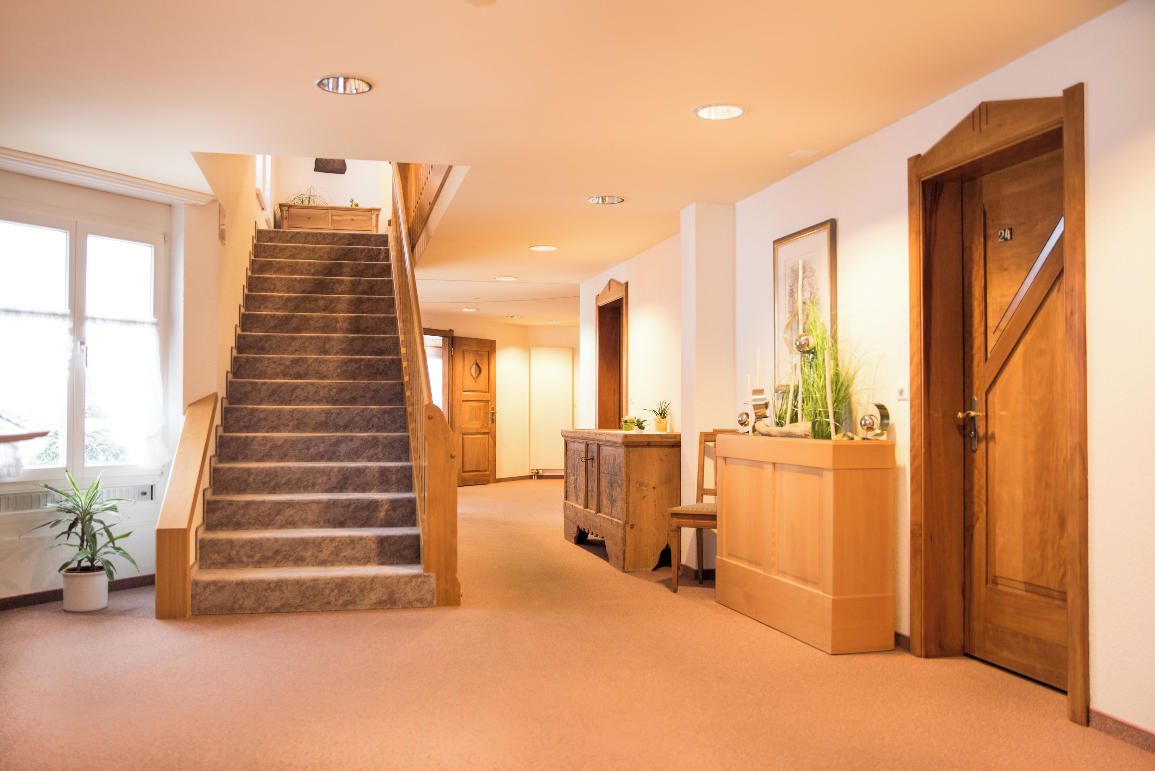 A staircase leading to a landing with a wooden door and a reception desk with a plant.