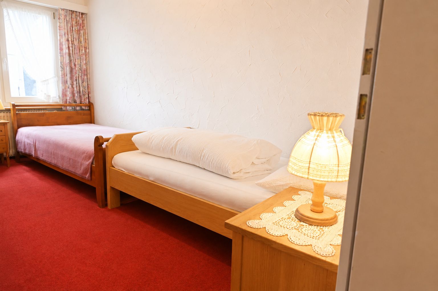 A single bed with a wooden frame, a bedside table with a lamp, and a window with curtains.