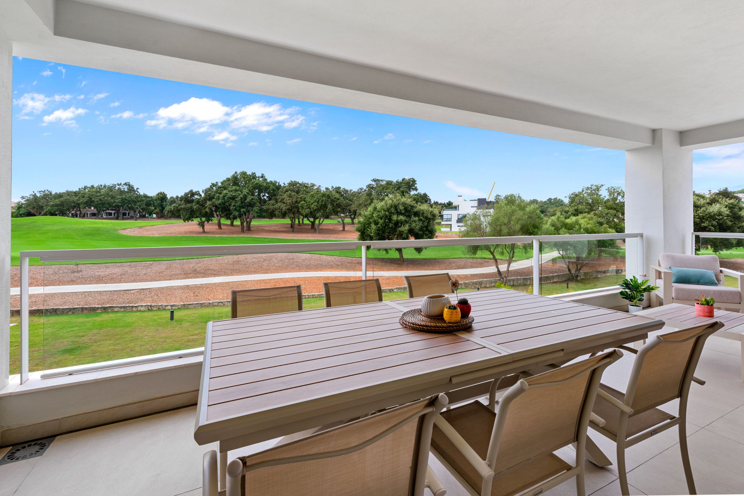 A balcony with a wooden table, chairs, and a view of a golf course.
