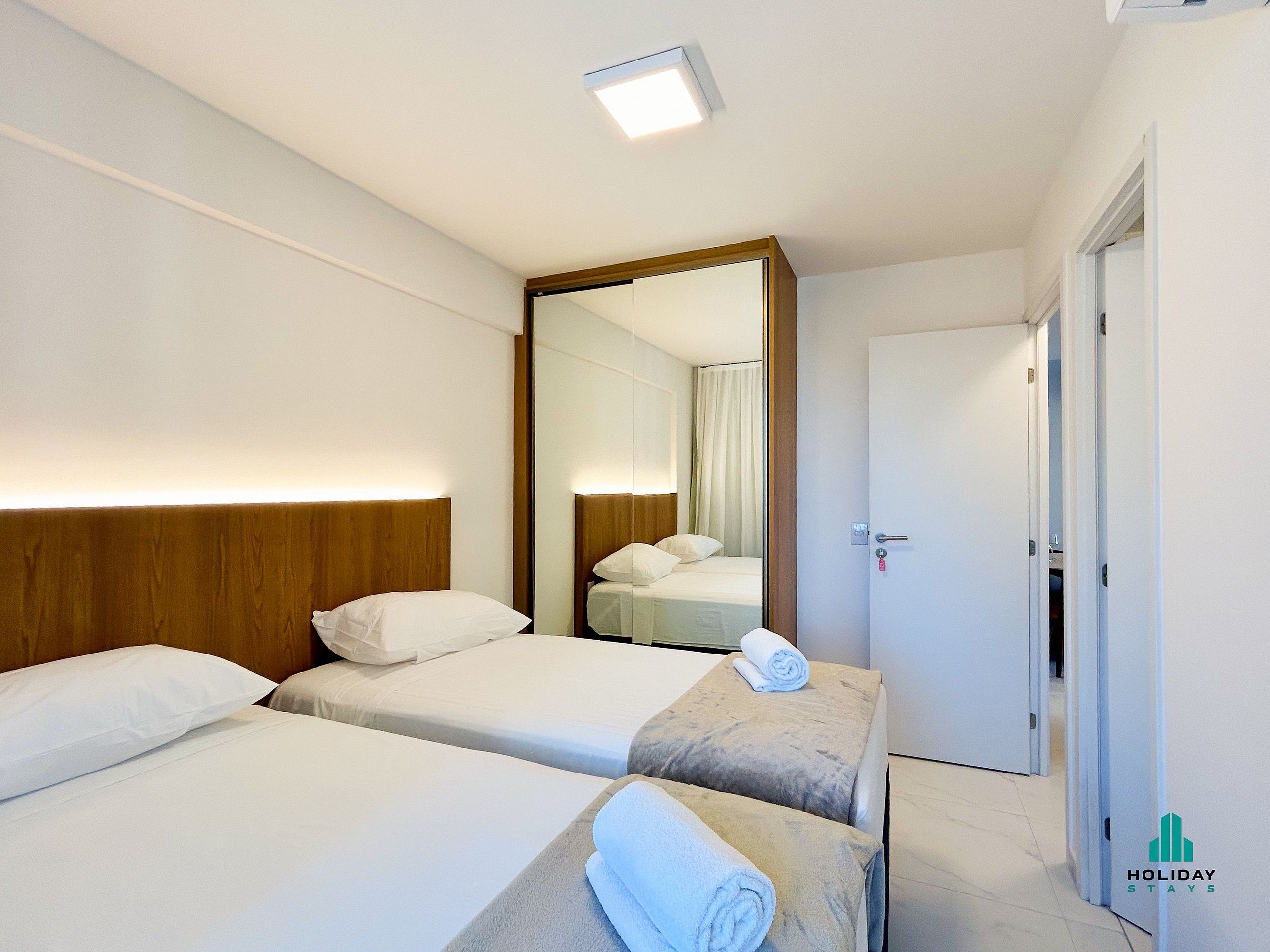 Habitación de hotel con dos camas, un espejo, una puerta y una lámpara en el techo.