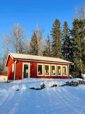 A red cabin with a tiled roof, surrounded by snow and trees. - Forest home with sauna by Dalälven in Hedesunda (Hedesunda)