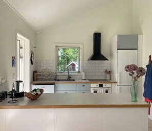 A modern kitchen with a central island, white cabinetry, a black range hood, and a view of greenery outside. - Forest home with sauna by Dalälven in Hedesunda (Hedesunda)