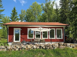 Un bâtiment rouge avec un toit en tuiles, de grandes fenêtres et une terrasse aménagée avec du mobilier d’extérieur.