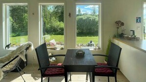 Uma sala de jantar com mesa e cadeiras, grandes janelas com vista para o verde e teto com vigas de madeira.