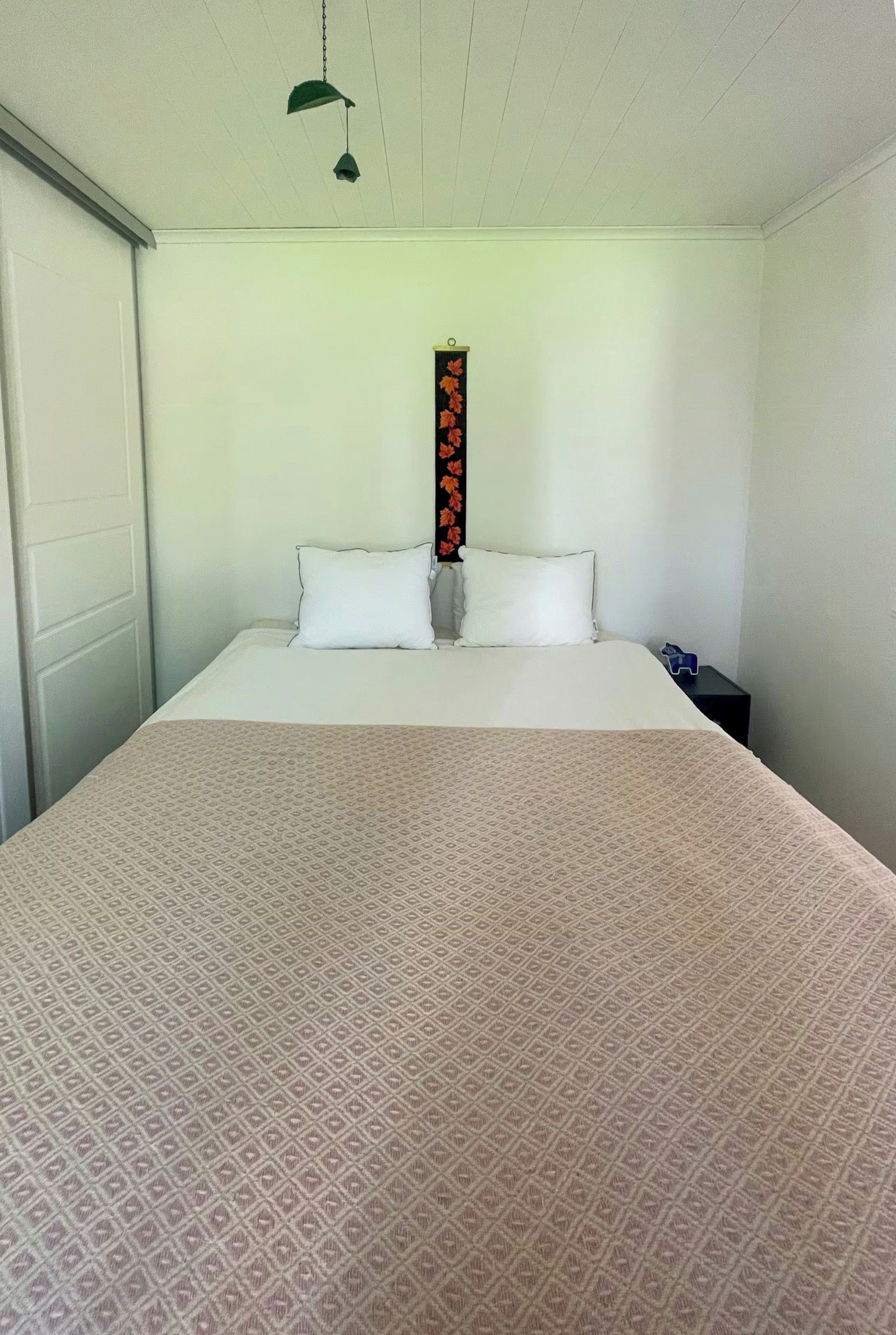 Un lit simple avec une couvre-lit à motifs, un objet décoratif fixé au mur et un luminaire suspendu.