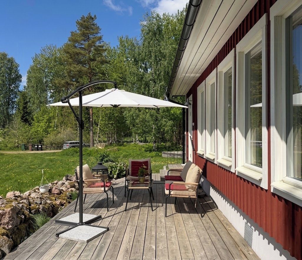 Une terrasse en bois avec des meubles d’extérieur, notamment des chaises et une table, ainsi qu’un parasol blanc.