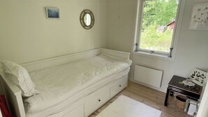 Quarto pequeno com uma cama de solteiro, janela, radiador e mesa de cabeceira.