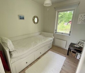 Une petite chambre avec un lit simple, une fenêtre, un radiateur et une table de chevet.