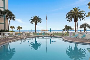A clear pool with lounge chairs and palm trees, a flag, and a view of the beach. - Private Beach • 3 Heated Pools • Ground Floor (Siesta Key)