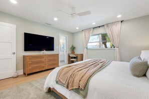 A bedroom with a bed, a TV, a desk, and a window with curtains. - Private Beach • 3 Heated Pools • Ground Floor (Siesta Key)