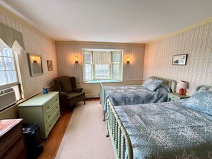 Ein Schlafzimmer mit zwei Betten, einem Schreibtisch, einem Stuhl, einem Fenster und Wandleuchten.
