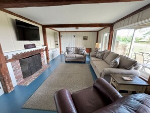 Ein Wohnzimmer mit Kamin, Sofas, Fernseher und Blick ins Freie.