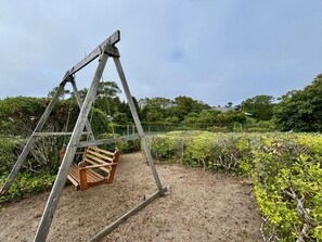 Ein hölzernes Schaukelgerüst in einem Garten mit Erdboden und verschiedenen Pflanzen.