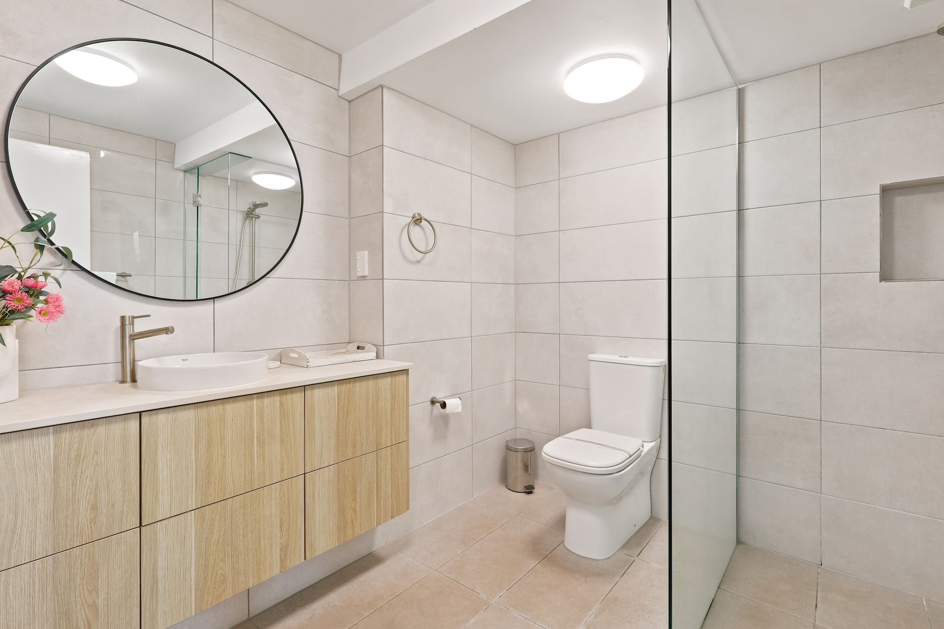 Un baño moderno con un espejo redondo, un lavabo, un inodoro y una zona de ducha.