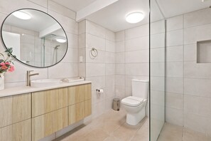 Ein modernes Badezimmer mit rundem Spiegel, Waschbecken, Toilette und Duschbereich.