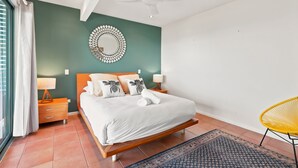 Ein Schlafzimmer mit einem Bett, Nachttischen, einem Deckenventilator, einer Wanddekoration und einem Sessel.