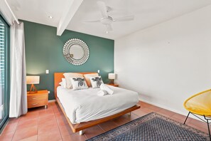 Ein Schlafzimmer mit einem Bett, Nachttischen, einem Deckenventilator, einer Wanddekoration und einem Sessel.