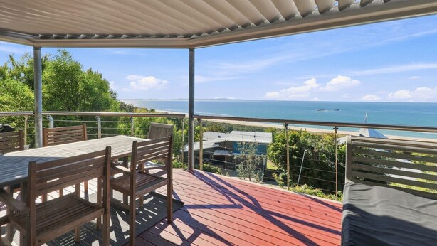 Ein überdachter Außenbereich mit Tisch und Stühlen mit Blick auf Strand und Meer.