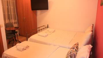Habitación de hotel con dos camas, un televisor montado en la pared, un armario de madera y una mesita con una silla.