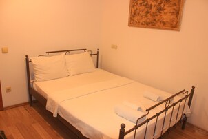 Una cama individual con estructura metálica, ropa de cama blanca y una toalla enrollada en el reposapiés.