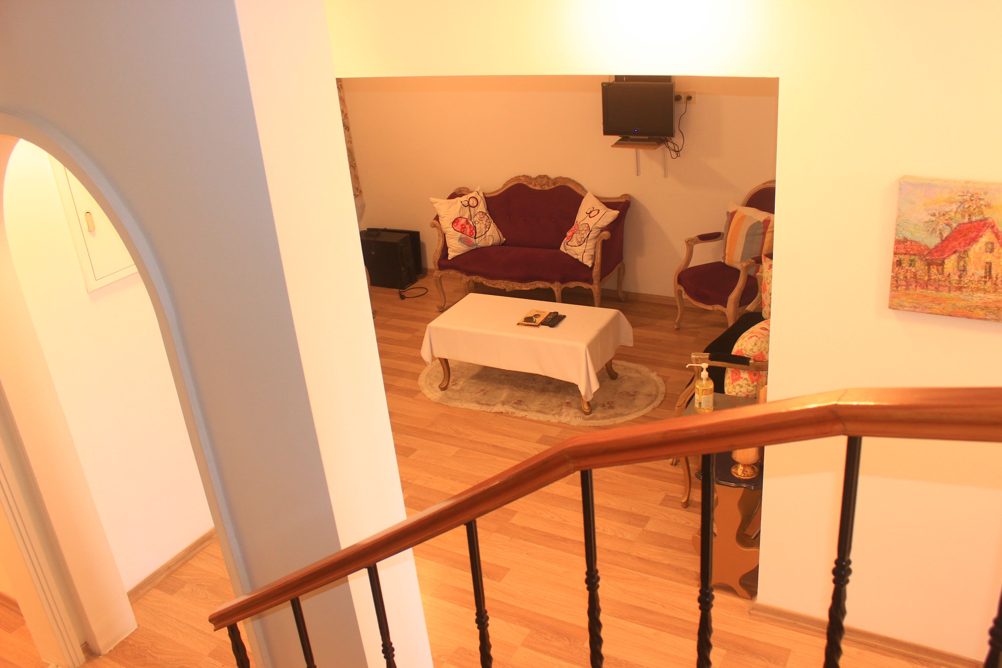Una escalera conduce a una sala de estar con un sofá rojo, una mesa blanca y un cuadro en la pared.