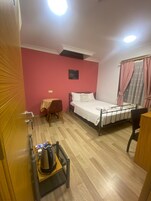 Habitación de hotel con cama, una mesita, una silla, un hervidor de agua y un ventanal con cortinas.