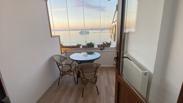 Un balcón con mesa y sillas, con vista a una masa de agua y un horizonte urbano distante.