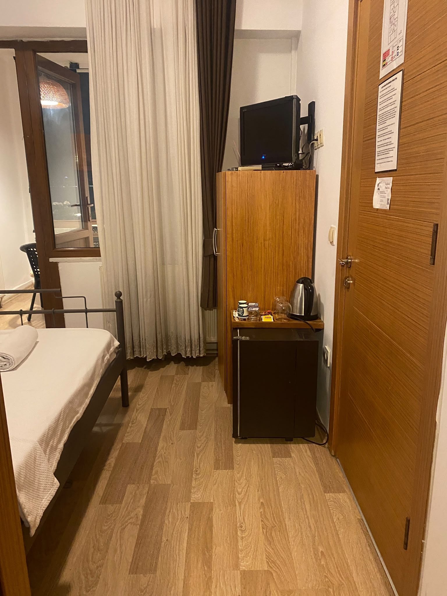 Habitación de hotel con cama, armario de madera, una mesita con tetera y televisor encima del armario.