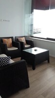 Una habitación con muebles de mimbre, una mesa de vidrio y una ventana con vistas a un edificio.