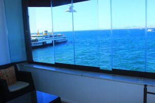 Una habitación con un ventanal grande que da a una masa de agua, una silla y una mesa.