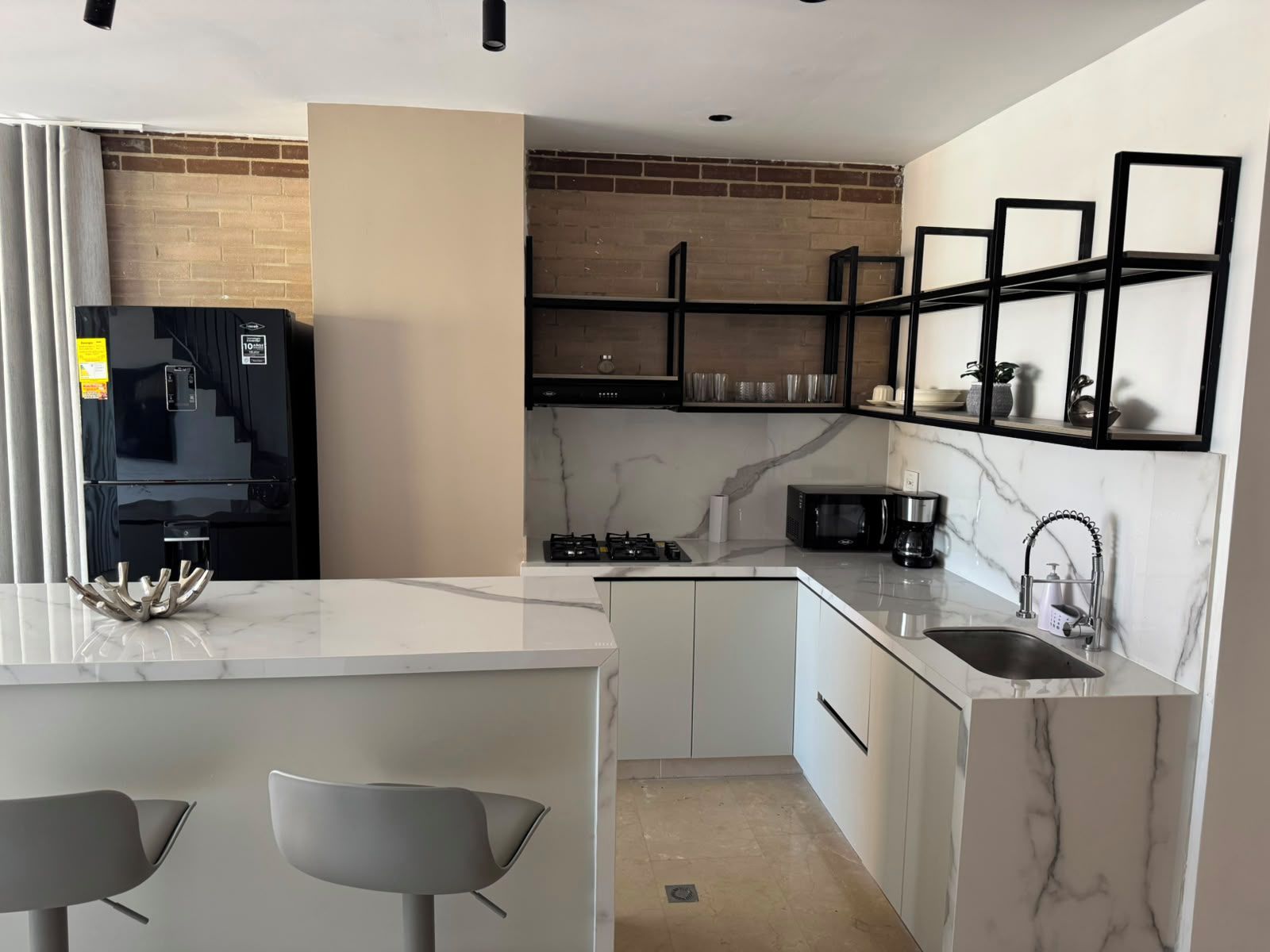 Una cocina moderna con encimera de mármol, estufa empotrada, refrigerador negro y un lavamanos con grifo.