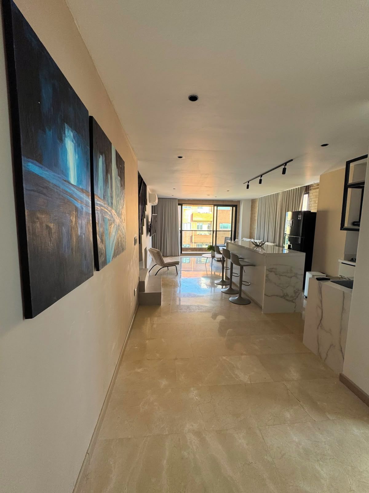 A modern interior with a kitchen area, dining space, and a hallway leading to a balcony.