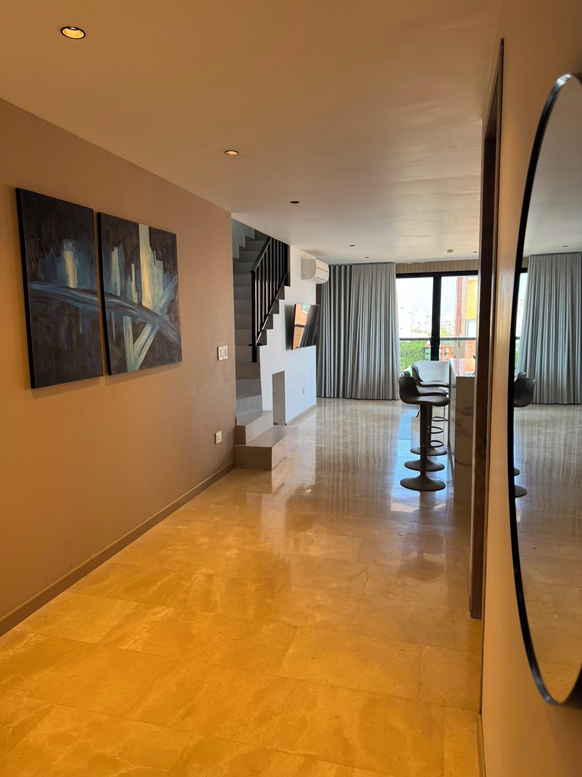 Un interior moderno con una escalera, una zona de comedor con taburetes de bar y obras de arte en las paredes.