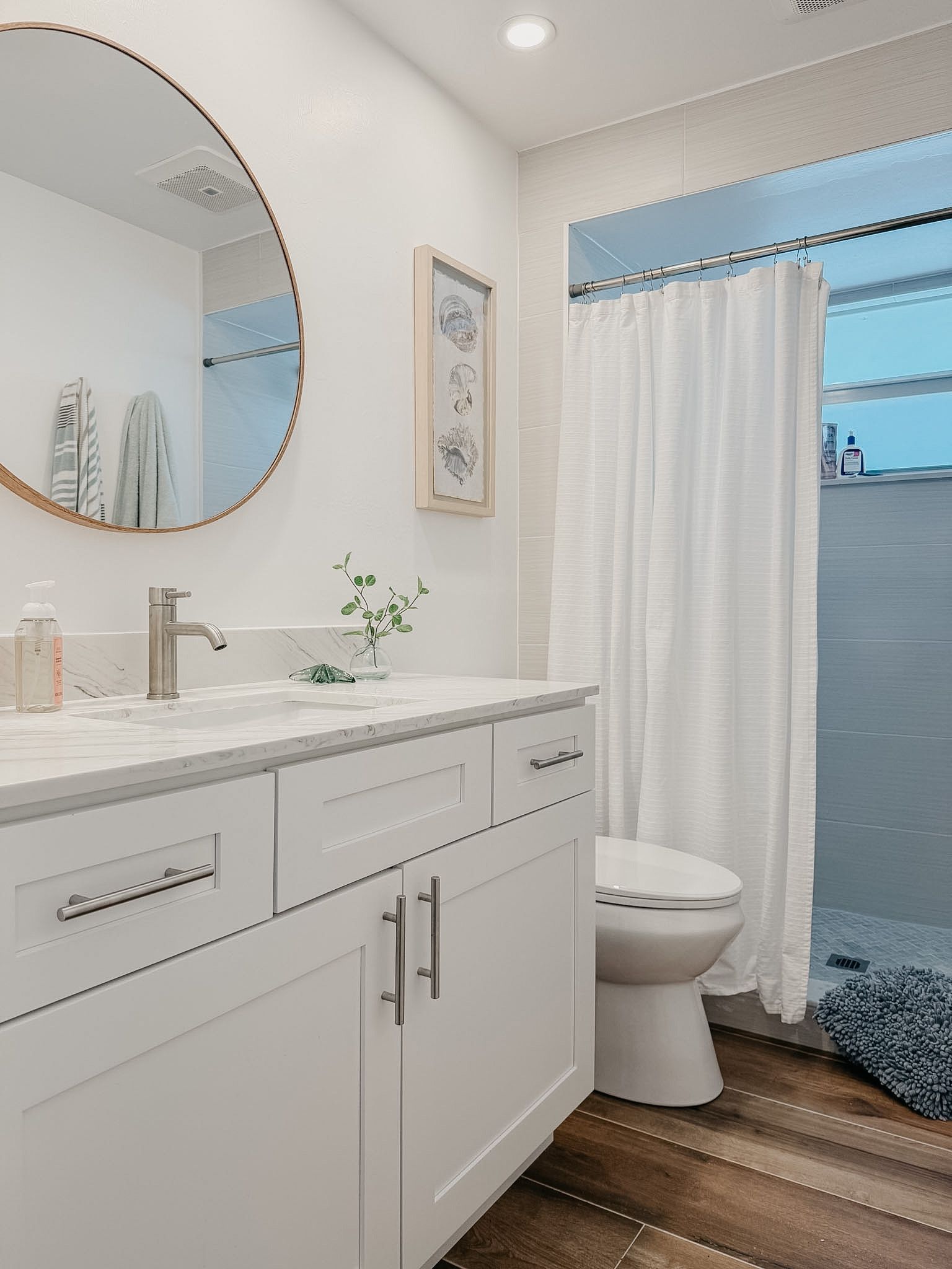 Een moderne badkamer met een witte wastafel, een ronde spiegel, een toilet en een douchegordijn.